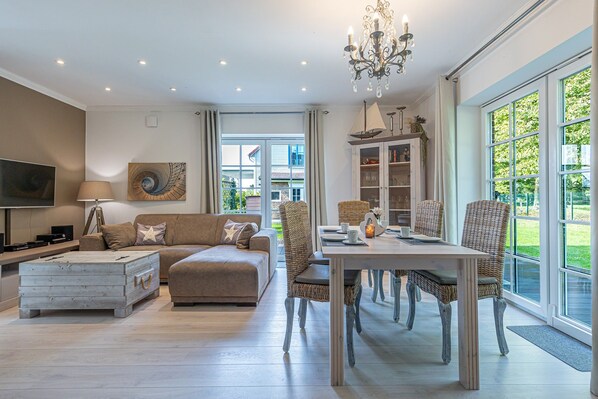 A spacious living room with a sofa, a coffee table, and a dining area with wicker chairs.