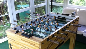 Une table de baby-foot en bois, dotée d’un plateau de jeu vert, posée sur un tapis vert.