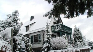 Une maison recouverte de neige, dotée d’un balcon, et des arbres également couverts de neige.