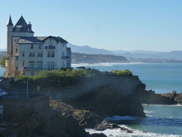 Een kustkasteel met meerdere verdiepingen, een balkon en uitzicht op zee en verafgelegen bergen.