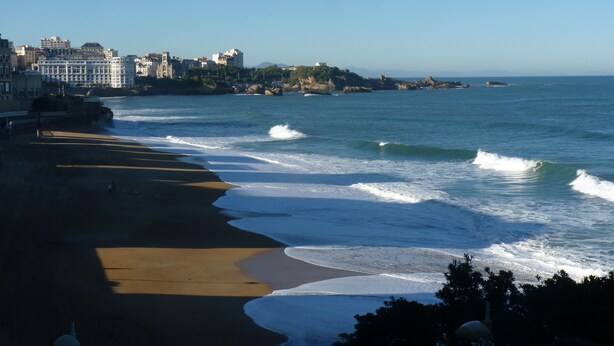 Un paysage urbain côtier avec une plage de sable, des vagues et une rangée de bâtiments le long de la côte.
