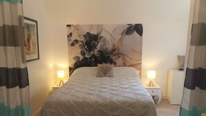 Un lit bien fait, recouvert d’une couette blanche, avec deux lampes de chevet, une œuvre d’art encadrée au mur et une peinture abstraite moderne au-dessus du lit.