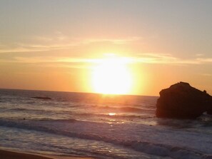Ein Sonnenuntergang über dem Meer mit einer großen Felsformation rechts.