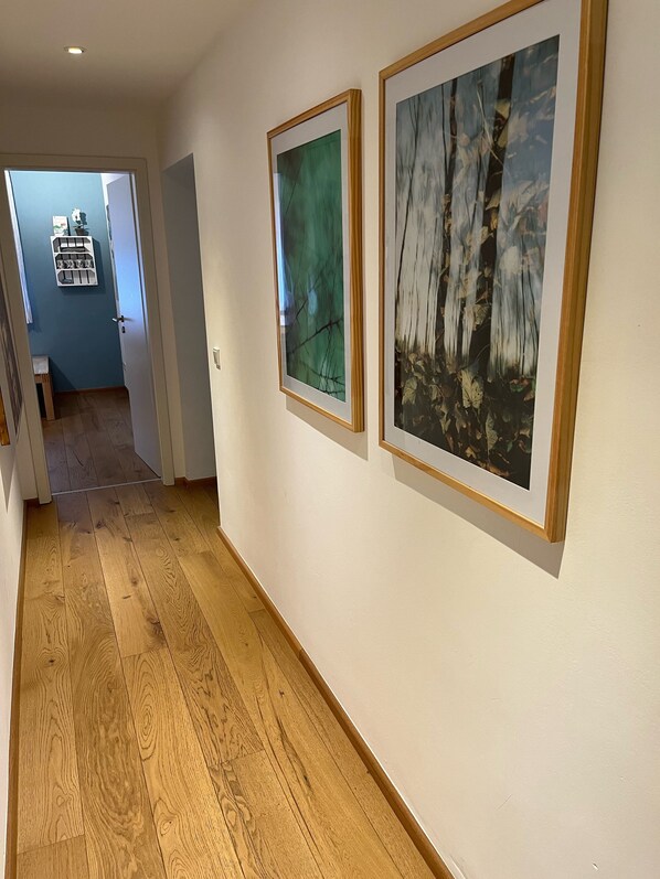 A hallway with wooden flooring, two framed artworks on the wall, and a door leading to another room. - Relaxation near Cologne in the middle of nature (Rösrath)