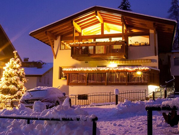 A two-story wooden building with balconies, snow-covered surroundings, and a car parked in front.
