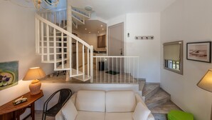 A modern interior with a staircase, a white sofa, a wooden table, and a green ottoman.