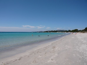 Een strand met helder turquoise water, een zandstrand en enkele mensen in de verte.