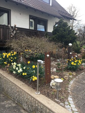 A garden with yellow and white flowers, a metal fence, and a house with a tiled roof. - Apartment for 2 - 8 people, ideal for 2 families with children  (Ehingen)