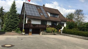 Een huis met twee verdiepingen, een schuin dak, zonnepanelen en een vlaggenmast.
