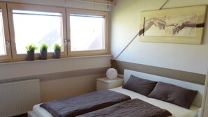 Een slaapkamer met een bed, nachtkastje, potplanten en een schilderij aan de muur.