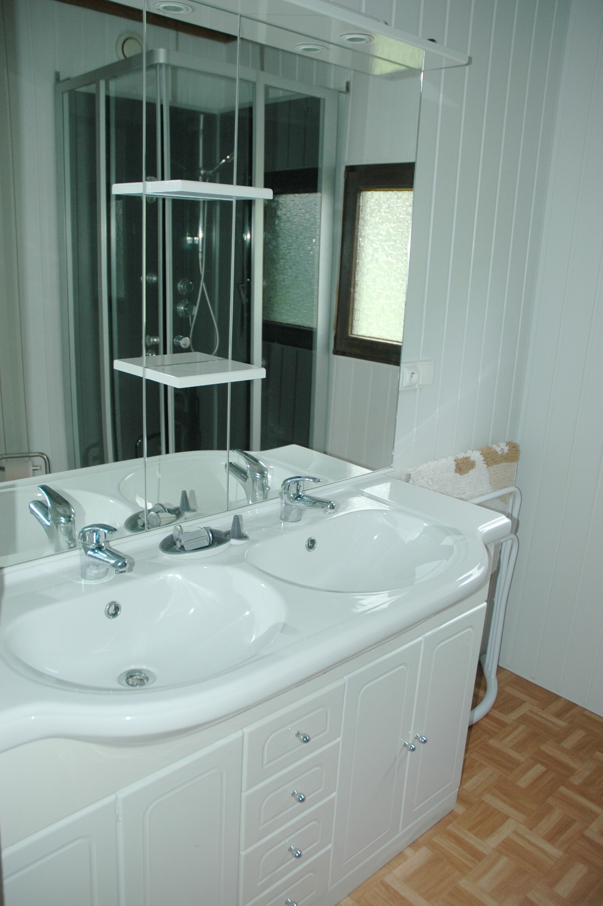 Une salle de bain avec deux lavabos, une étagère en verre et une fenêtre.