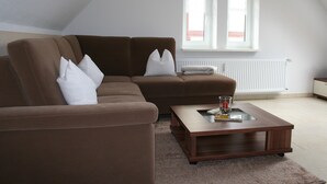 A living room with a brown sofa, a coffee table, and a window with white blinds. - Apartment Rudolphi (Wernigerode)