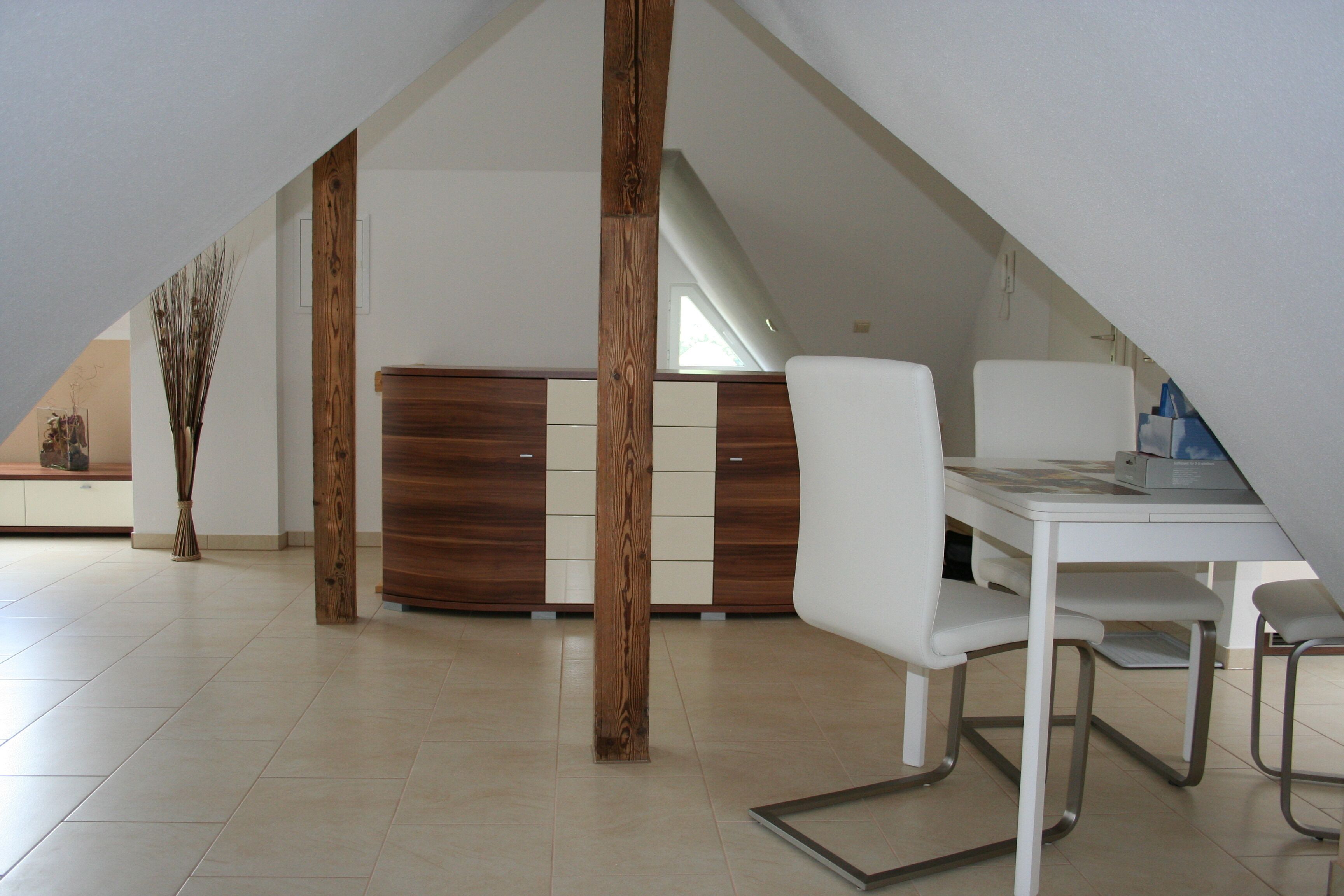 A modern dining area with a white table and chairs, a wooden cabinet, and a vase of dried plants.