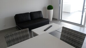 A modern living room with a black sofa, a white coffee table, and two wicker chairs. - BEAUTIFUL APARTMENT IN RESIDENCE STANDING UP BEAUTIFUL SEA AND MOUNTAIN (L'île-Rousse)
