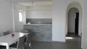 A modern kitchen with a stone backsplash, white cabinets, and a dining area with wicker chairs and a white table. - BEAUTIFUL APARTMENT IN RESIDENCE STANDING UP BEAUTIFUL SEA AND MOUNTAIN (L'île-Rousse)