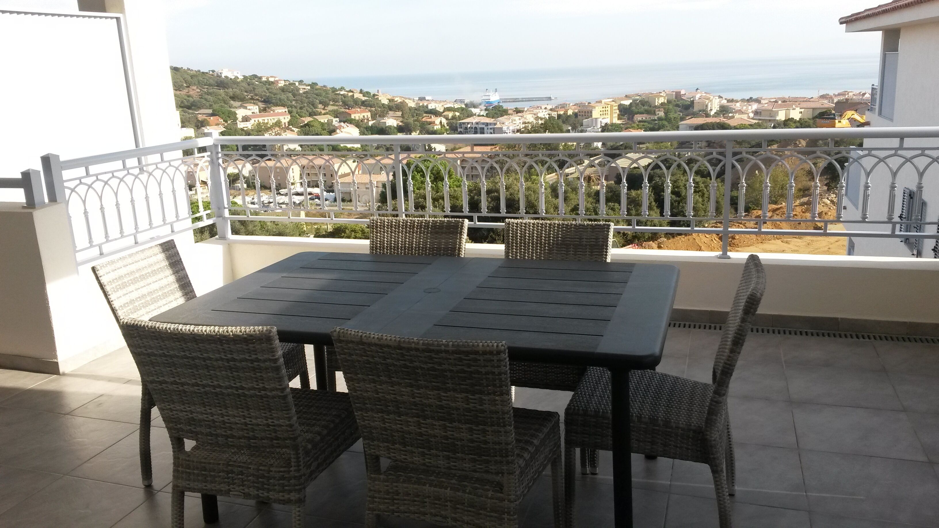En balkon med et bord og stole, der kigger ud over en kystby.