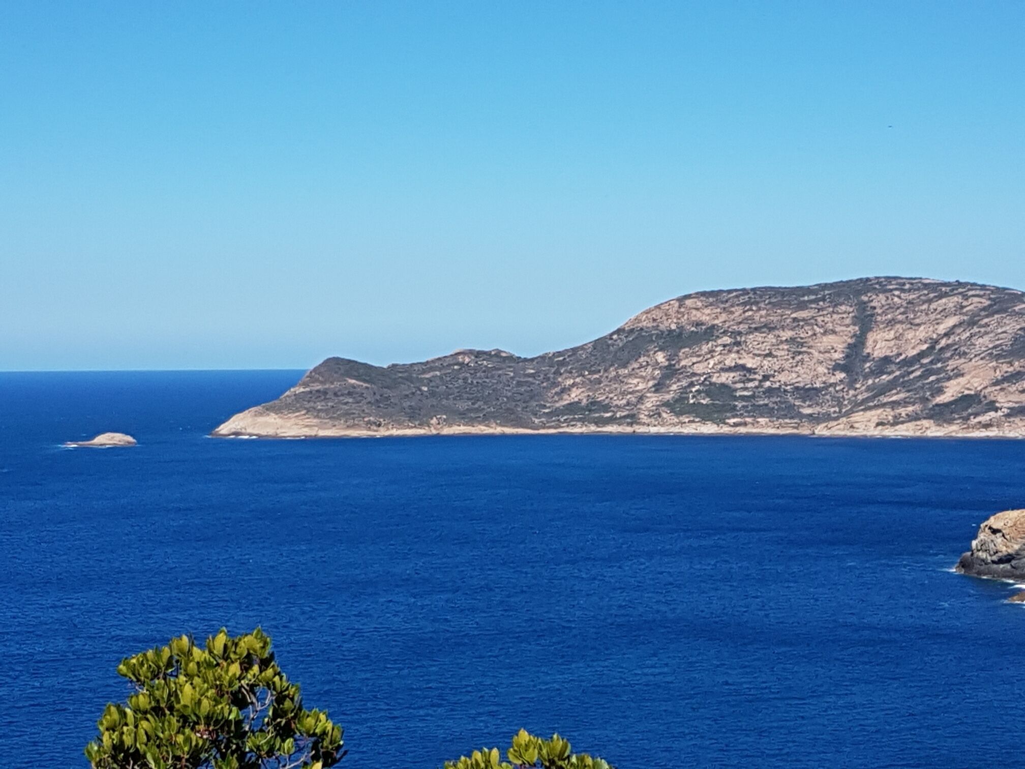 A coastal landscape with a prominent hill and clear blue sea.