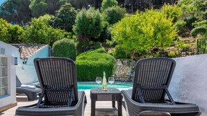 A poolside area with two wicker lounge chairs and a small table, a bottle of wine, and a glass. - Typical white Andalusian house in the heart of PUEBLO, with swimming pool and jacuzzi (Alhaurín el Grande)