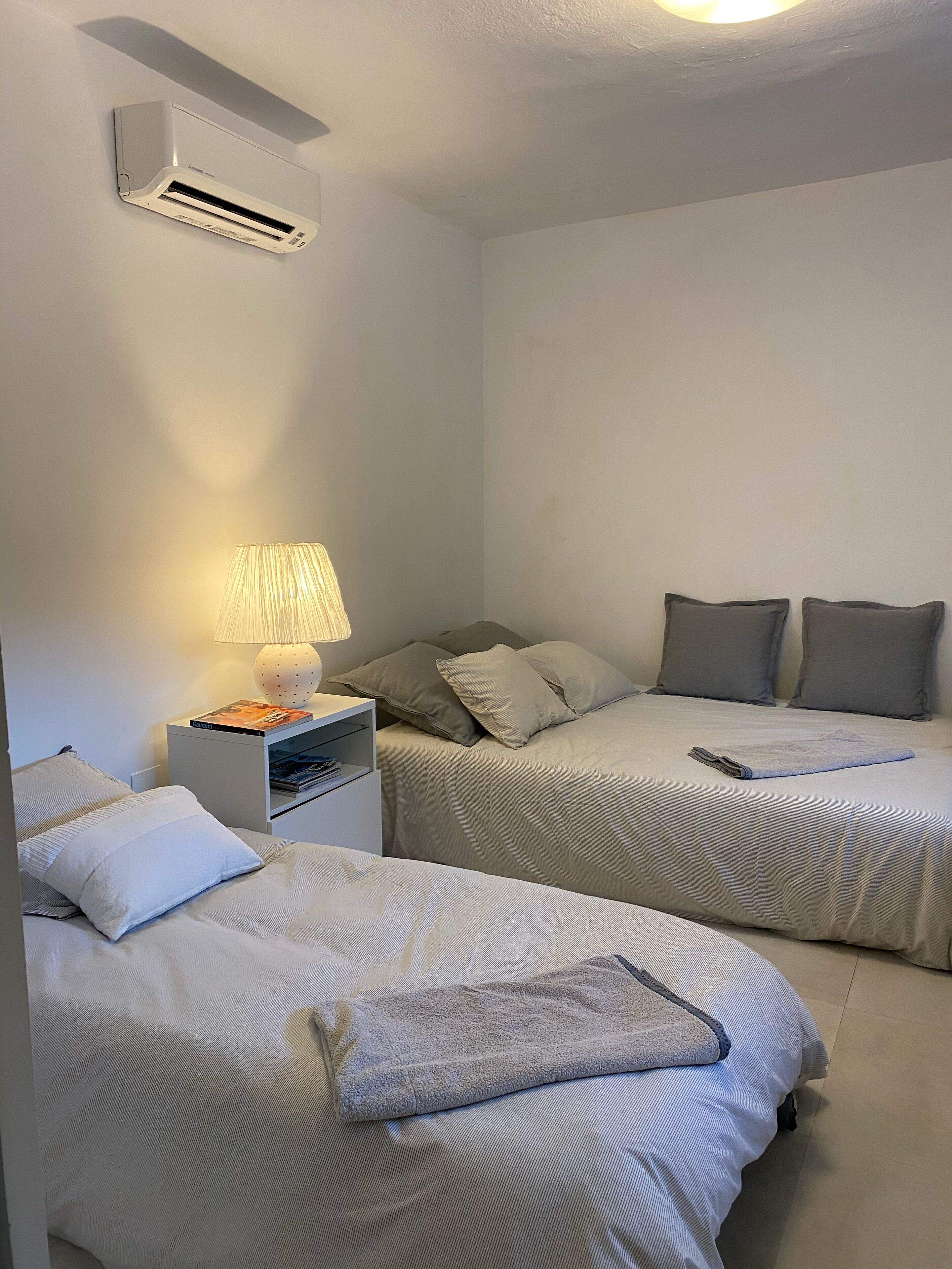 Ein Schlafzimmer mit zwei Betten, einem Nachttisch mit Lampe und einer Wandklimaanlage.