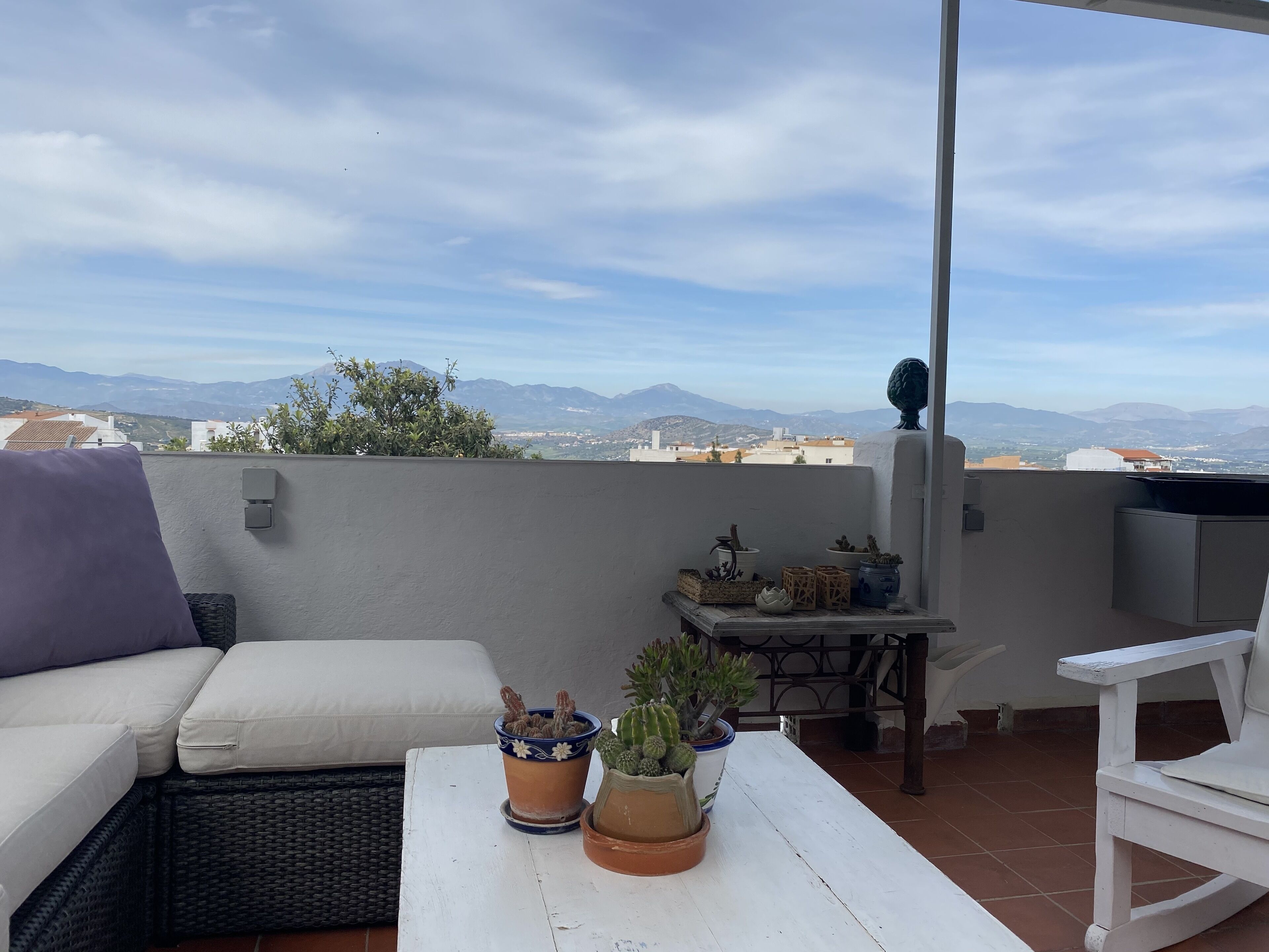 Une terrasse sur le toit avec un canapé blanc, une petite table agrémentée de plantes en pot et une vue sur les montagnes lointaines.