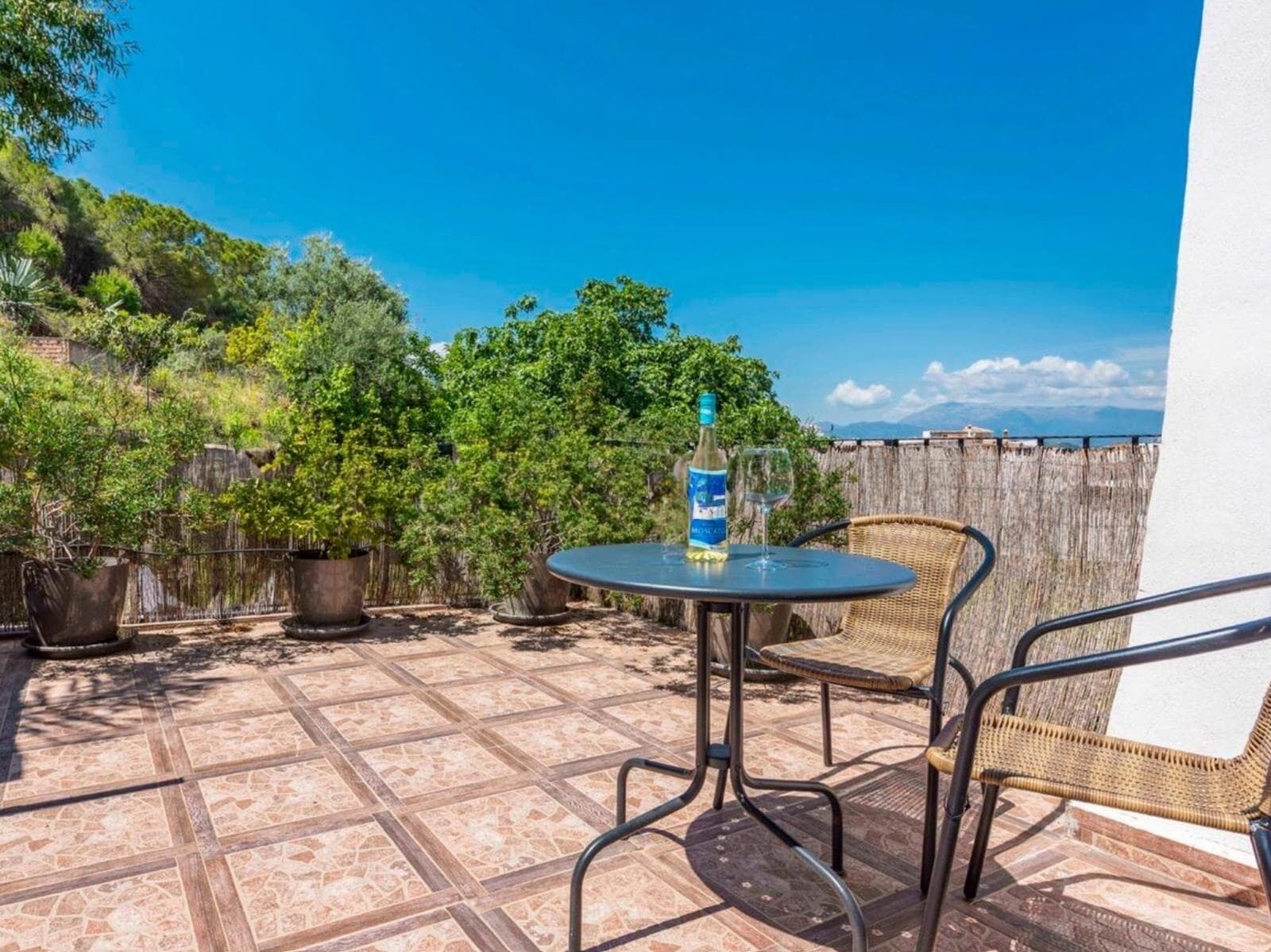 A patio with a round table and two wicker chairs, a bottle of water, and a glass on the table.