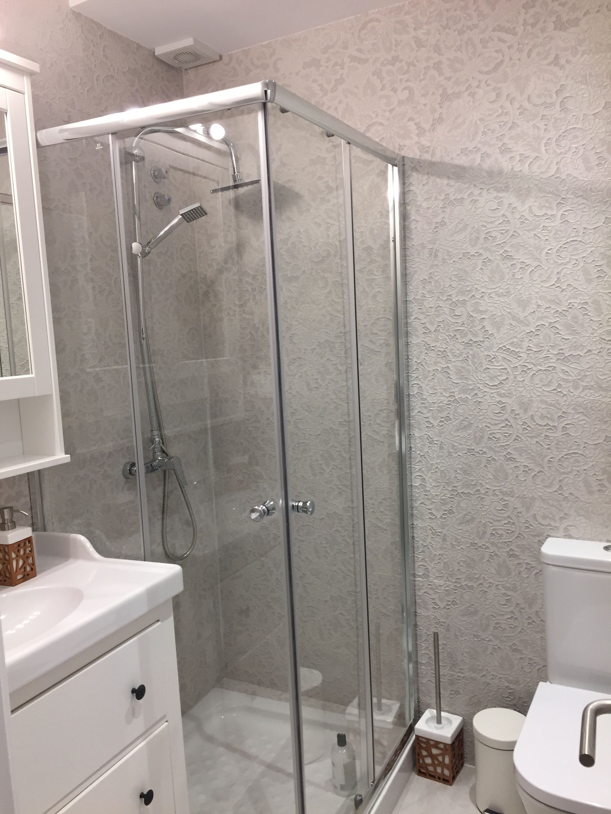 A modern bathroom with a glass-enclosed shower, a white sink, and a toilet.