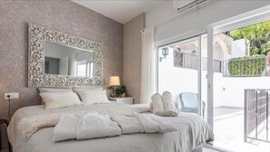 A bedroom with a large bed, a decorative mirror, a nightstand, and a view of a balcony. - Typical white Andalusian house in the heart of PUEBLO, with swimming pool and jacuzzi (Alhaurín el Grande)