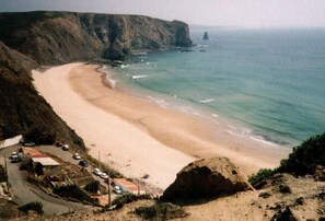A coastal road leading to a beach with a cliff on one side and a rocky outcrop on the other.