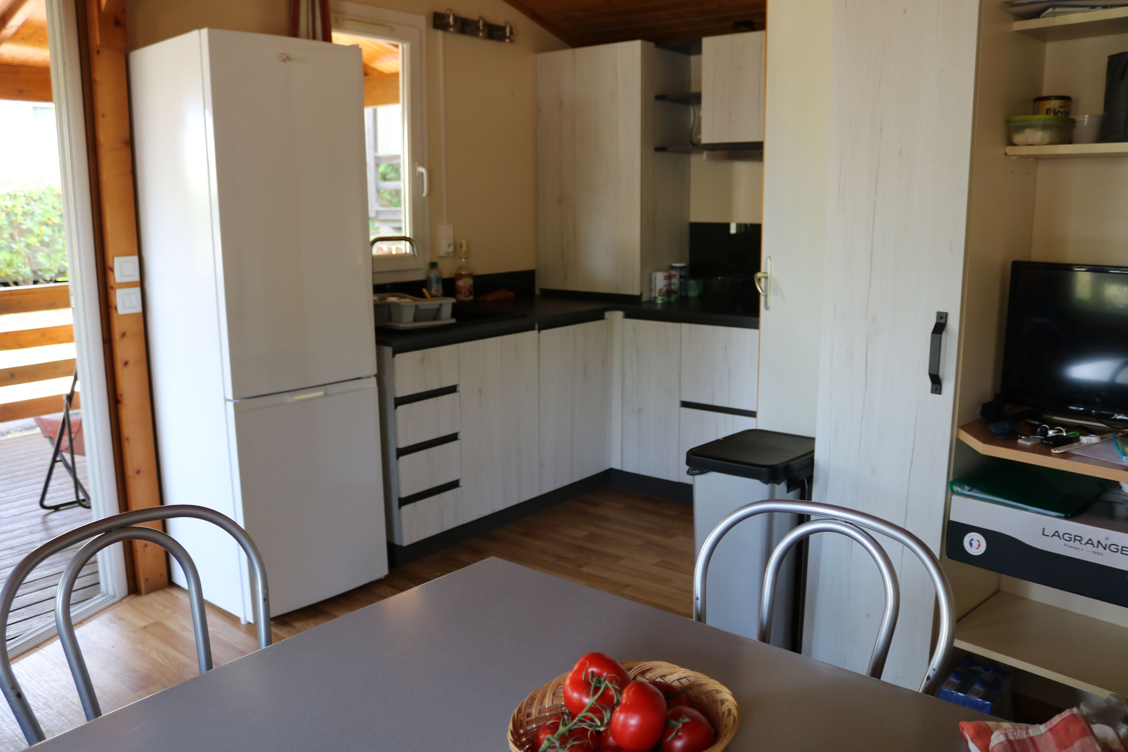 A compact kitchen with white cabinets, a refrigerator, a dining table with chairs, and a television on a stand.