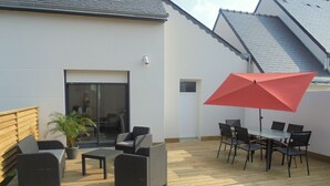Une terrasse avec des meubles d’extérieur, un parasol rouge et une plante en pot.