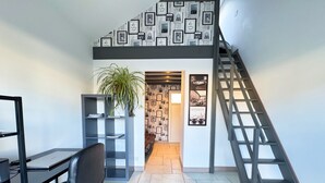 Un espace de bureau moderne comprenant un bureau, une chaise, une étagère, une plante en pot, des tableaux encadrés accrochés au mur et un escalier.