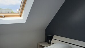 Une chambre à coucher avec un lit, une table de chevet, une lampe et une lucarne.