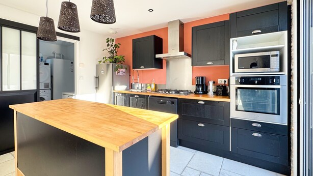 Une cuisine moderne dotée d’un îlot central, de meubles noirs, d’appareils électroménagers en acier inoxydable et de luminaires suspendus.