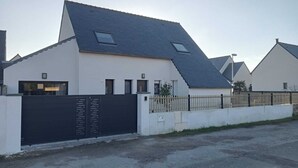 Une maison moderne avec un toit en pente, une allée bordée d’une grille et une façade blanche.
