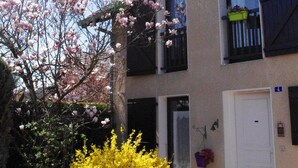 Un edificio de dos pisos con balcones, una puerta y un pequeño jardín con árboles florecientes.