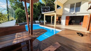 A wooden deck with a swimming pool, lounge chairs, and a dog. - Unique in Guadeloupe: Villa 400 m from the beach with mango tree house (Le Gosier)