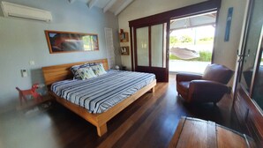 A bedroom with a wooden bed, a chair, a window with a view, and a ceiling fan. - Unique in Guadeloupe: Villa 400 m from the beach with mango tree house (Le Gosier)