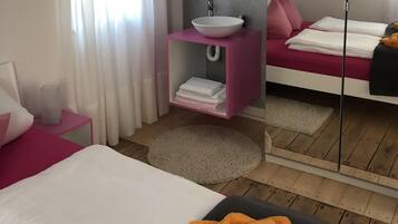 A modern bedroom with a bed, a bedside table, a mirror, a vanity with a sink, and a large mirror.