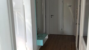 Käytävä, jossa on puulattia, valkoiset seinät ja lasihyllykkö.