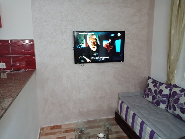 Un téléviseur à écran plat fixé au mur dans un salon, avec un canapé et une table basse.