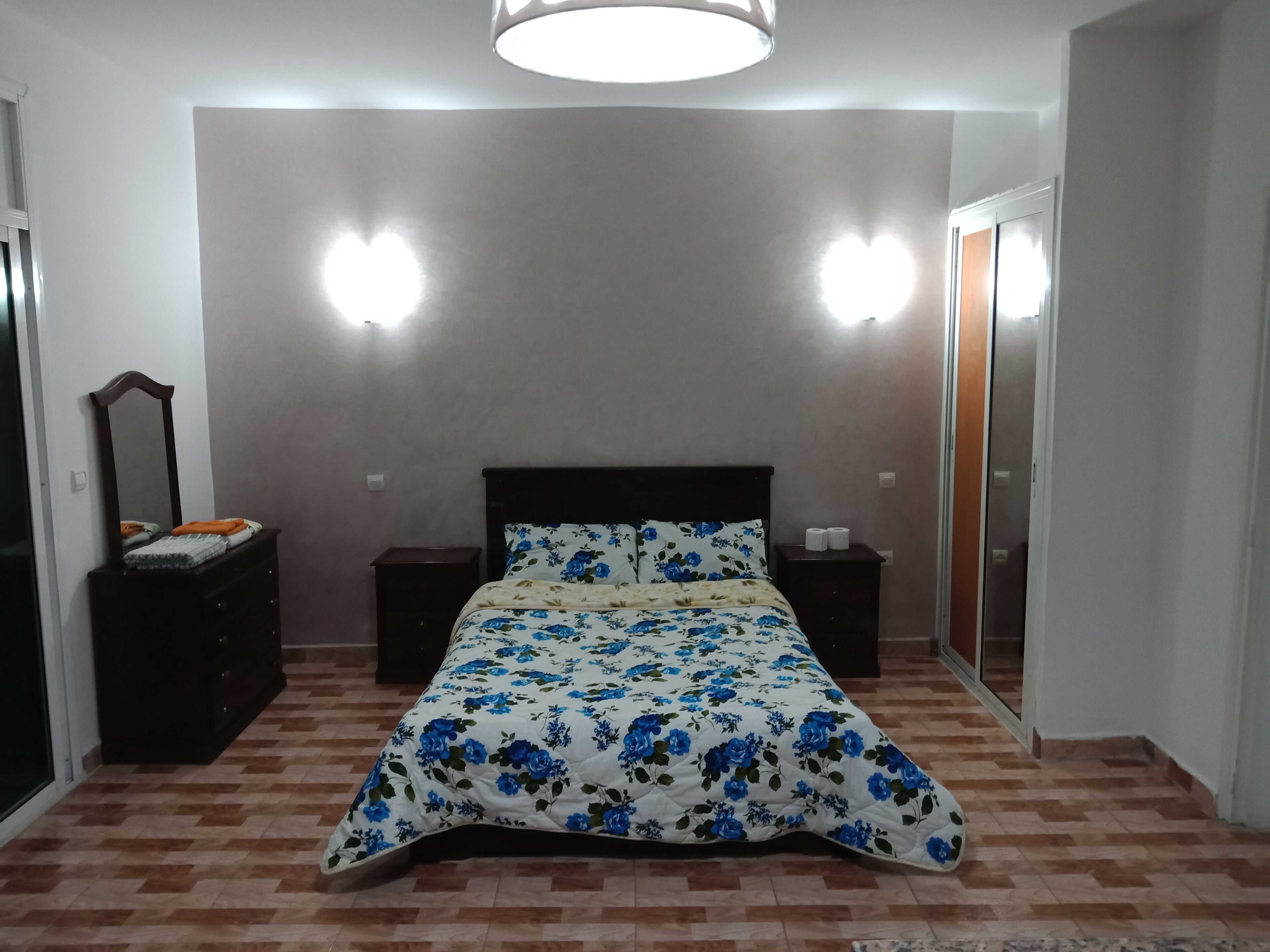 A bedroom with a bed, two bedside tables, a dresser, a mirror, and a wardrobe.