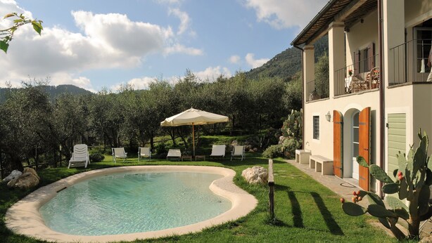 A pool with lounge chairs and a patio area, surrounded by greenery and a mountain backdrop.