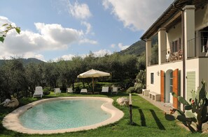 A pool with lounge chairs and a patio area, surrounded by greenery and a mountain backdrop. - Villa with private pool, garden, quality furnishings in a beautiful location. (Camaiore)