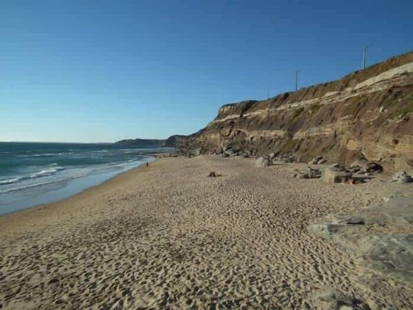 A sandy beach with a rocky cliff and a clear sky.