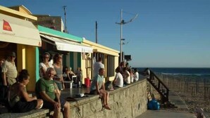 Eine Uferpromenade mit Menschen, die auf einer Steinsitzbank sitzen und auf das Meer blicken.