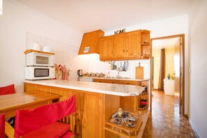 A compact kitchen with wooden cabinets, a white countertop, and a dining area with red chairs.