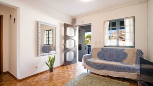 Ein Zimmer mit Holzboden, einer Couch mit gemustertem Bezug, einem Spiegel und einer Tür zu einem anderen Raum.