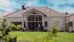 Een twee verdiepingen tellend huis met een pannendak, een garage en een voortuin met buitenmeubilair.