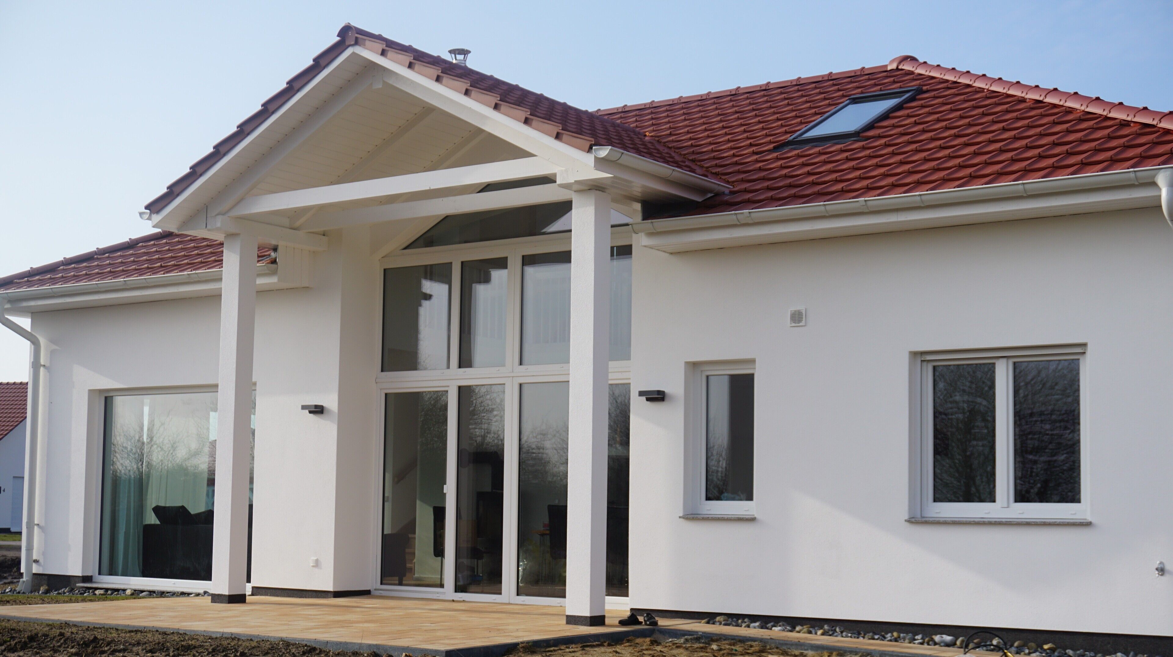 A modern two-story house with a white exterior, large sliding glass doors, and a red-tiled roof.