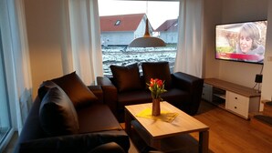 Een woonkamer met een bank, een salontafel met een bloemenvaas, een televisie en uitzicht op een besneeerd landschap door het raam.